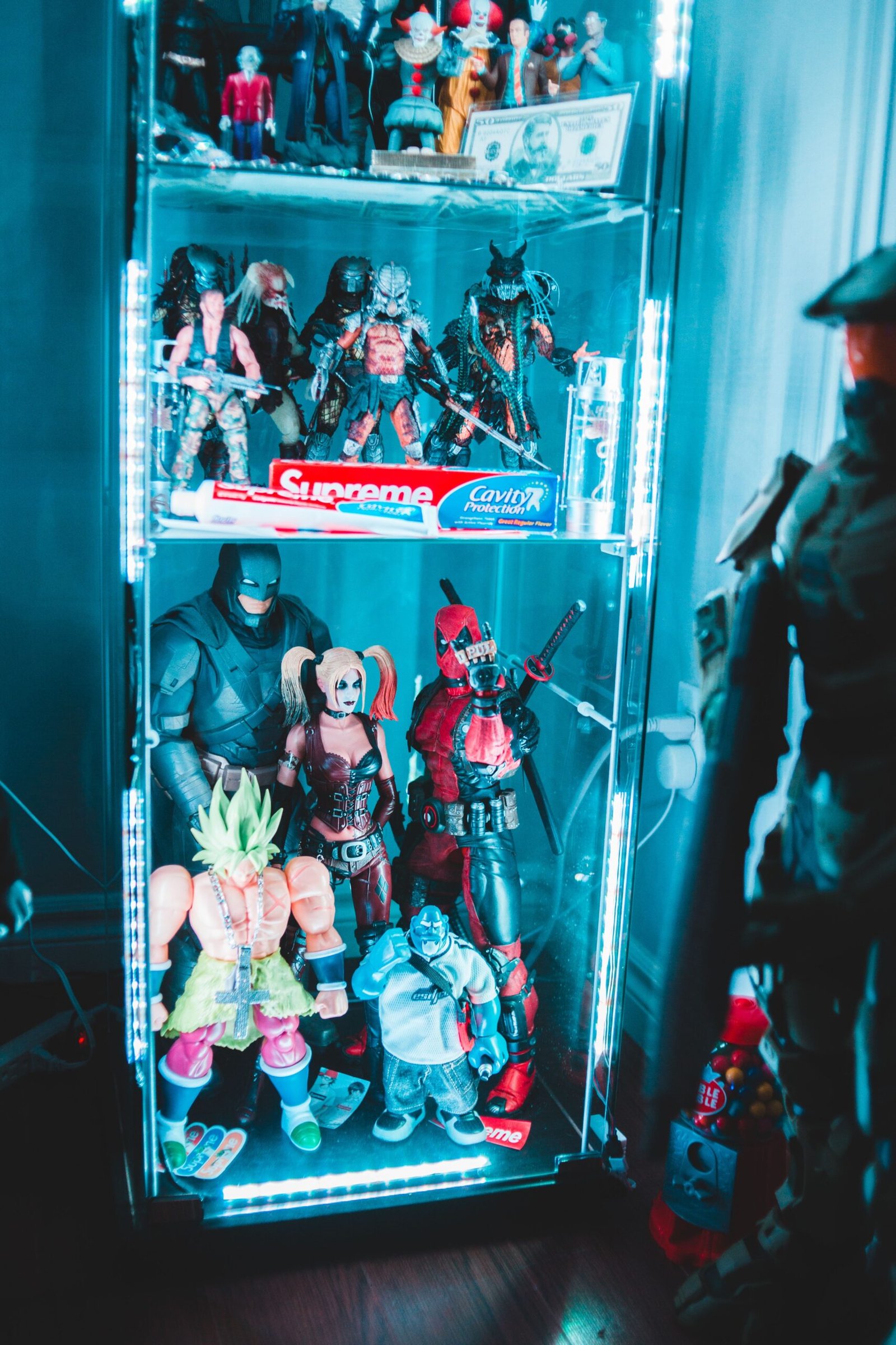 Display cabinet filled with collectible action figures from Marvel, DC, Predator, Batman, Deadpool, and other pop culture franchises.